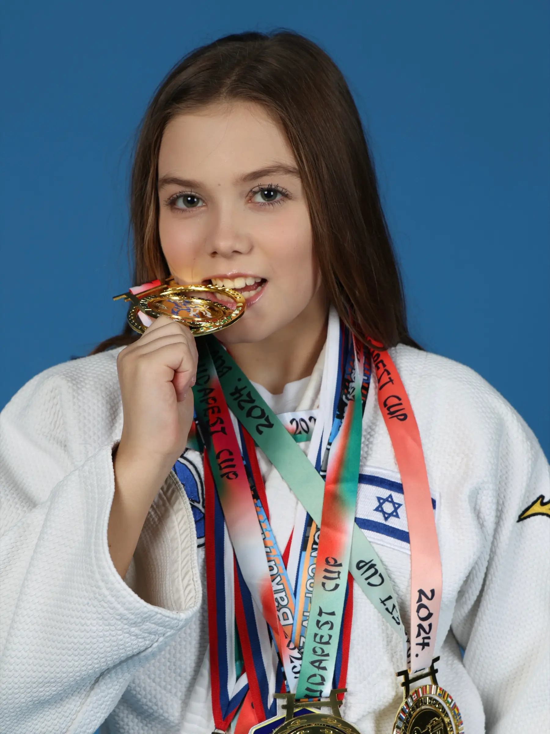 Melissa Safronsky biting a gold medal, in a judo suit against a blue background