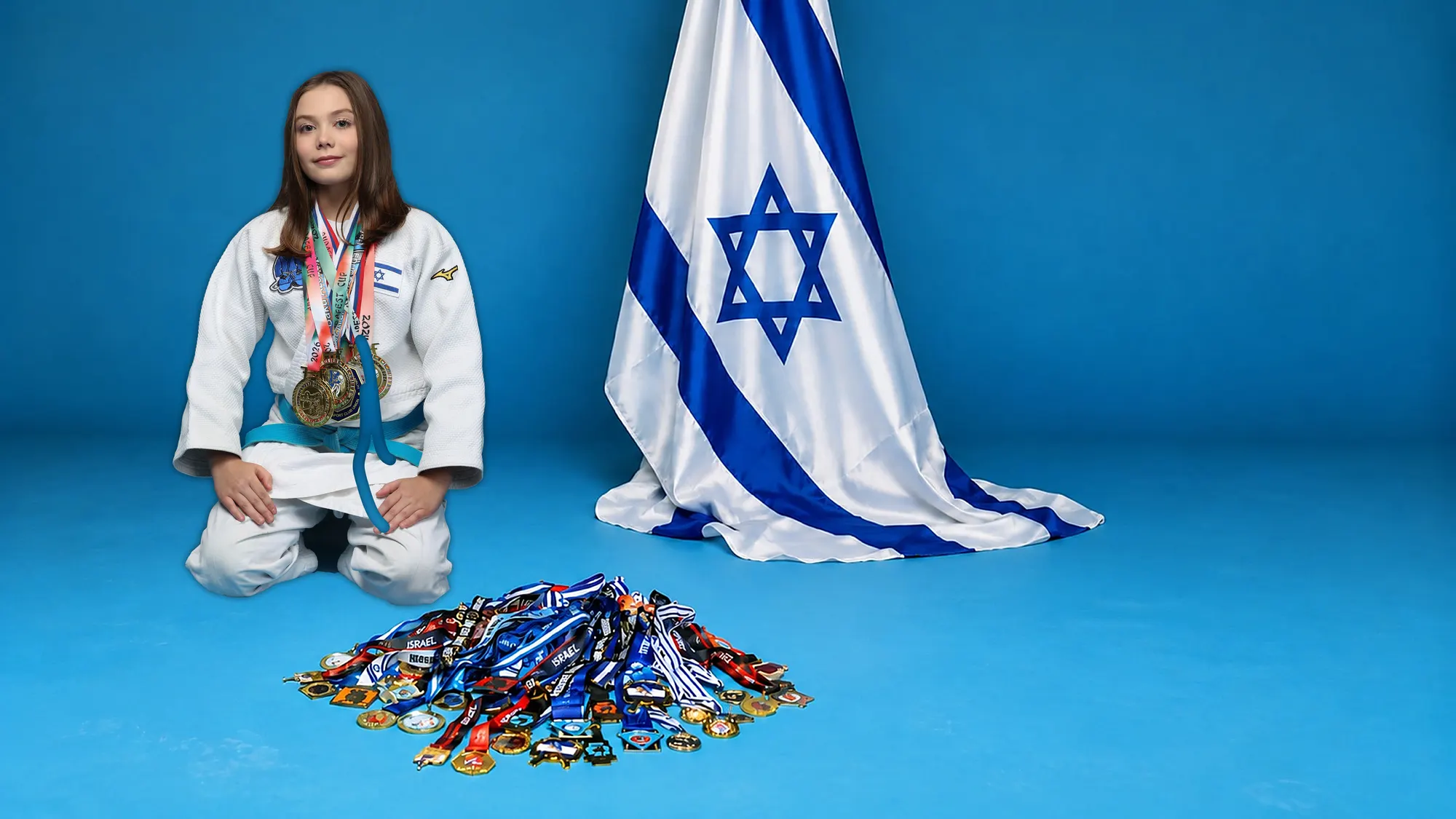 Melissa Safronsky kneeling in a judo suit with medals on her chest, next to an Israeli flag and a pile of medals