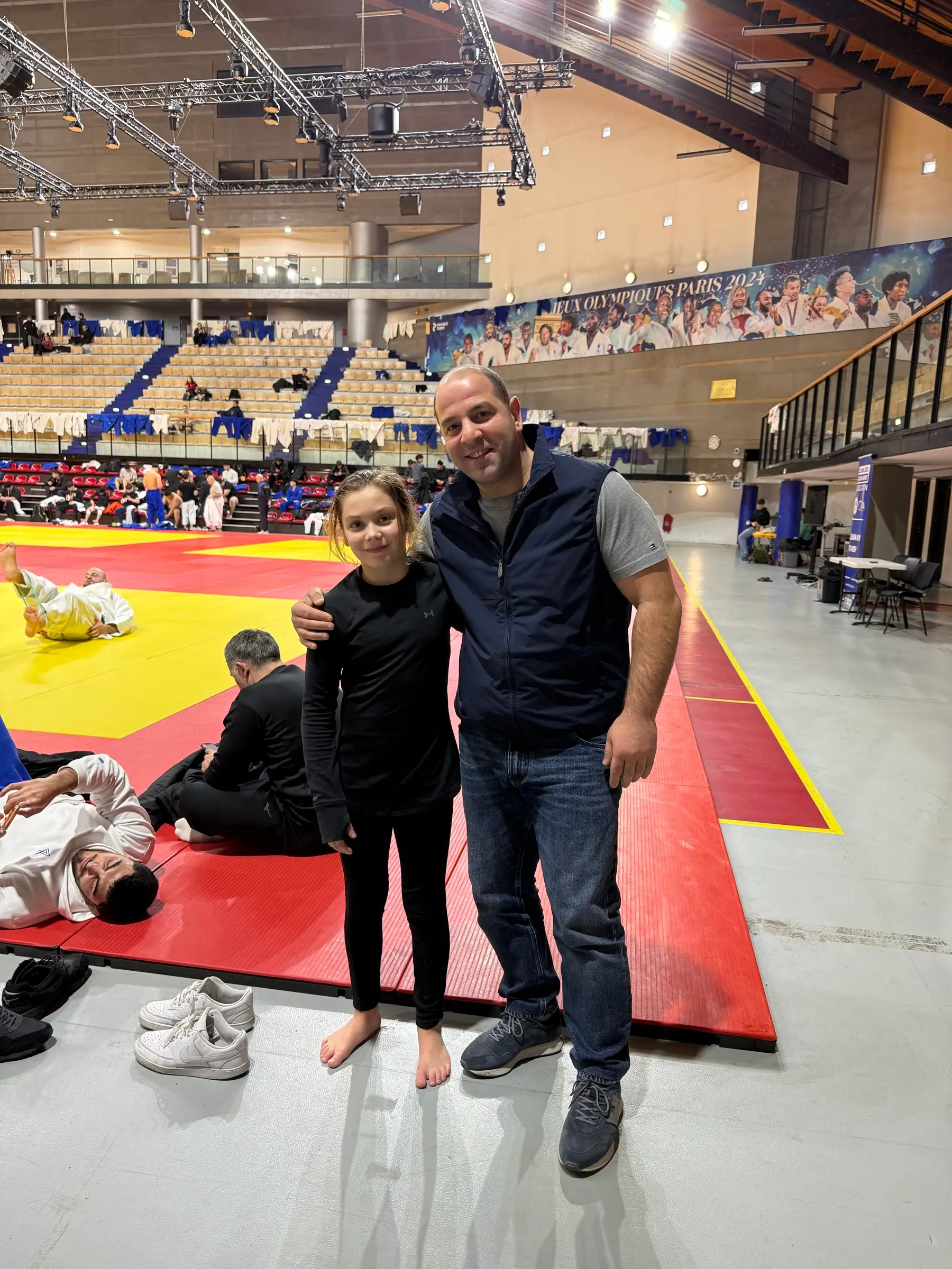 Melissa and a man in a blue vest on the hall’s mat