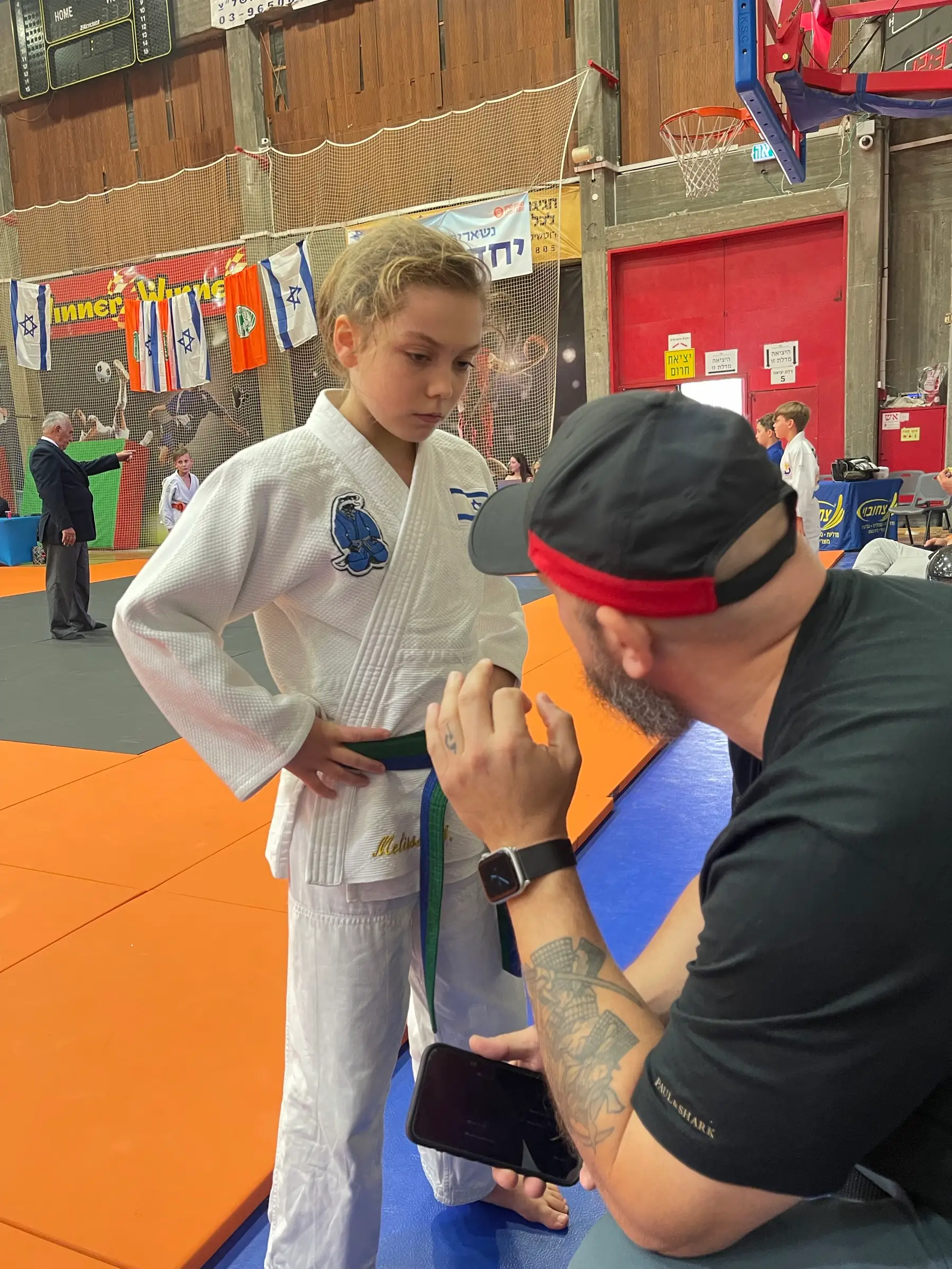 Melissa in a judo suit listening to her coach, who is wearing a cap, in a training hall