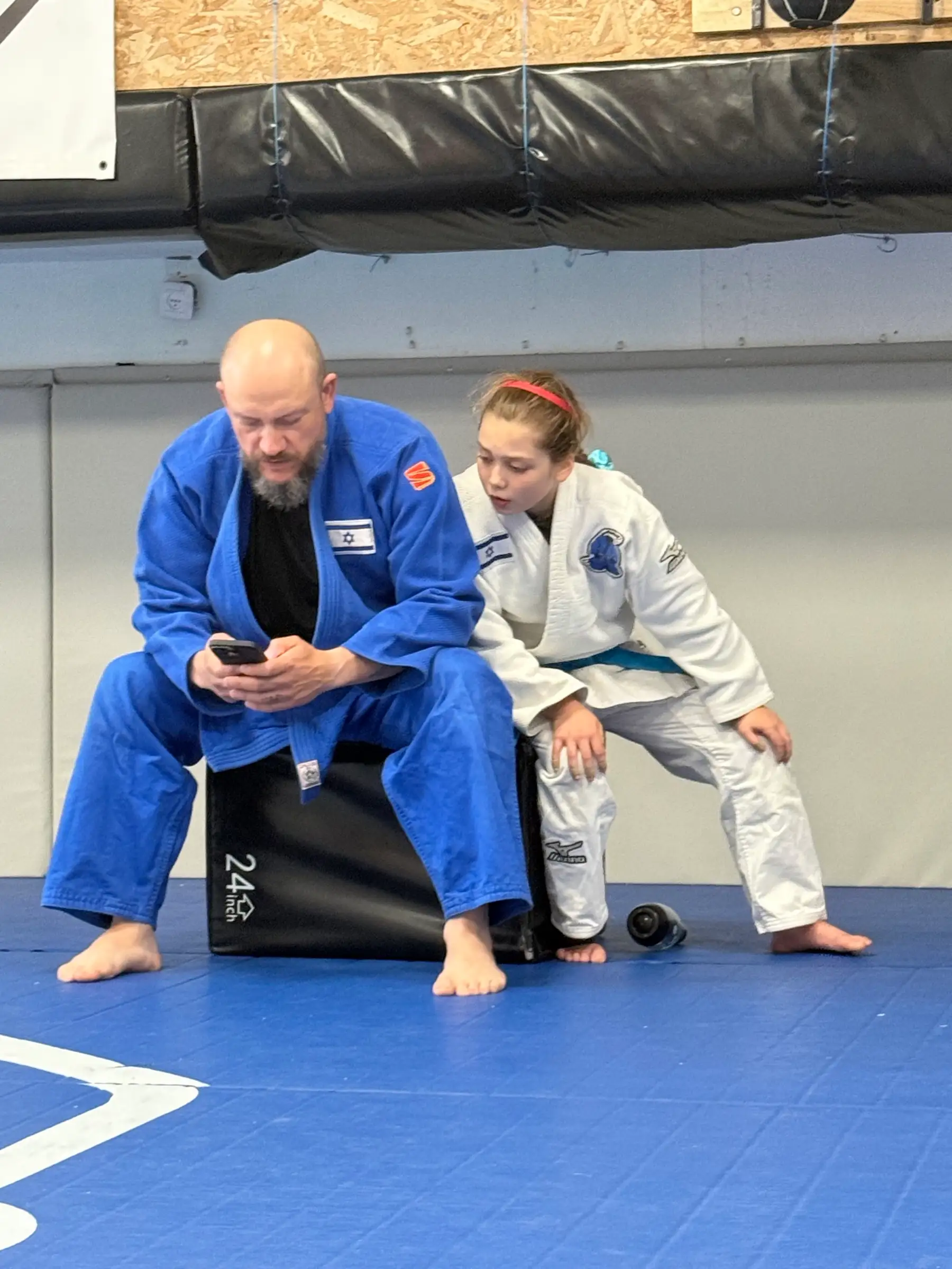 Melissa’s father with a phone in his hand, and Melissa waiting beside him on the mat